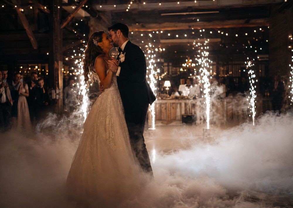 Couple sharing a close first dance surrounded by low dry ice fog and cold spark fountains in the background